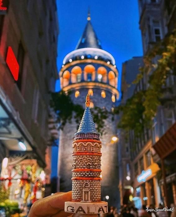 Hand holding a Galata Tower figurine in front of Galata Tower