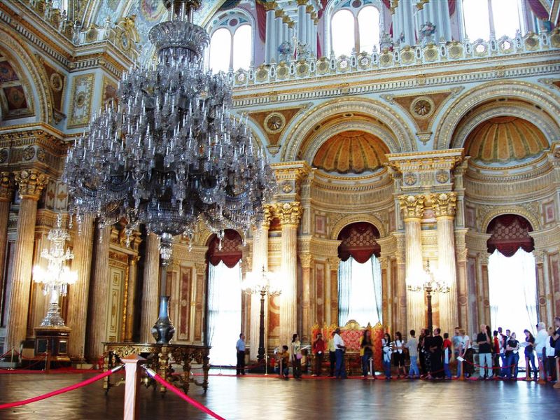 Large chandelier, people in background exploring the ornate palace interiors